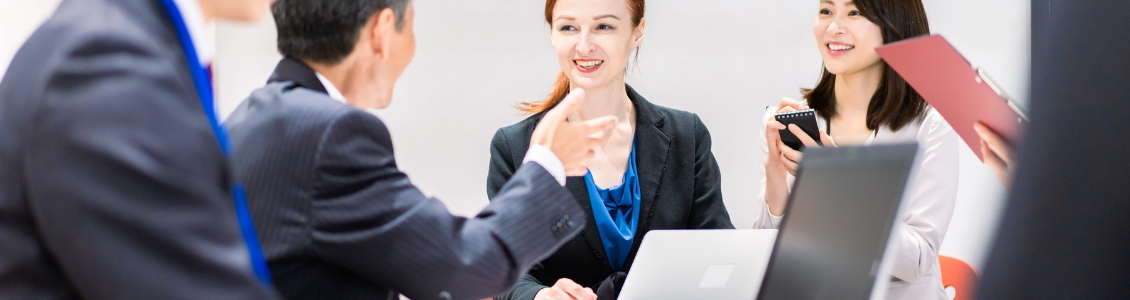 Zwei Männer und zwei Frauen in Businesskleidung sitzen an einem Tisch und haben eine Besprechung